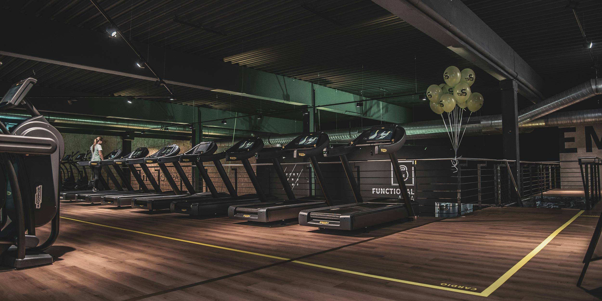 Gym interior with treadmills lined up under industrial ceiling lighting