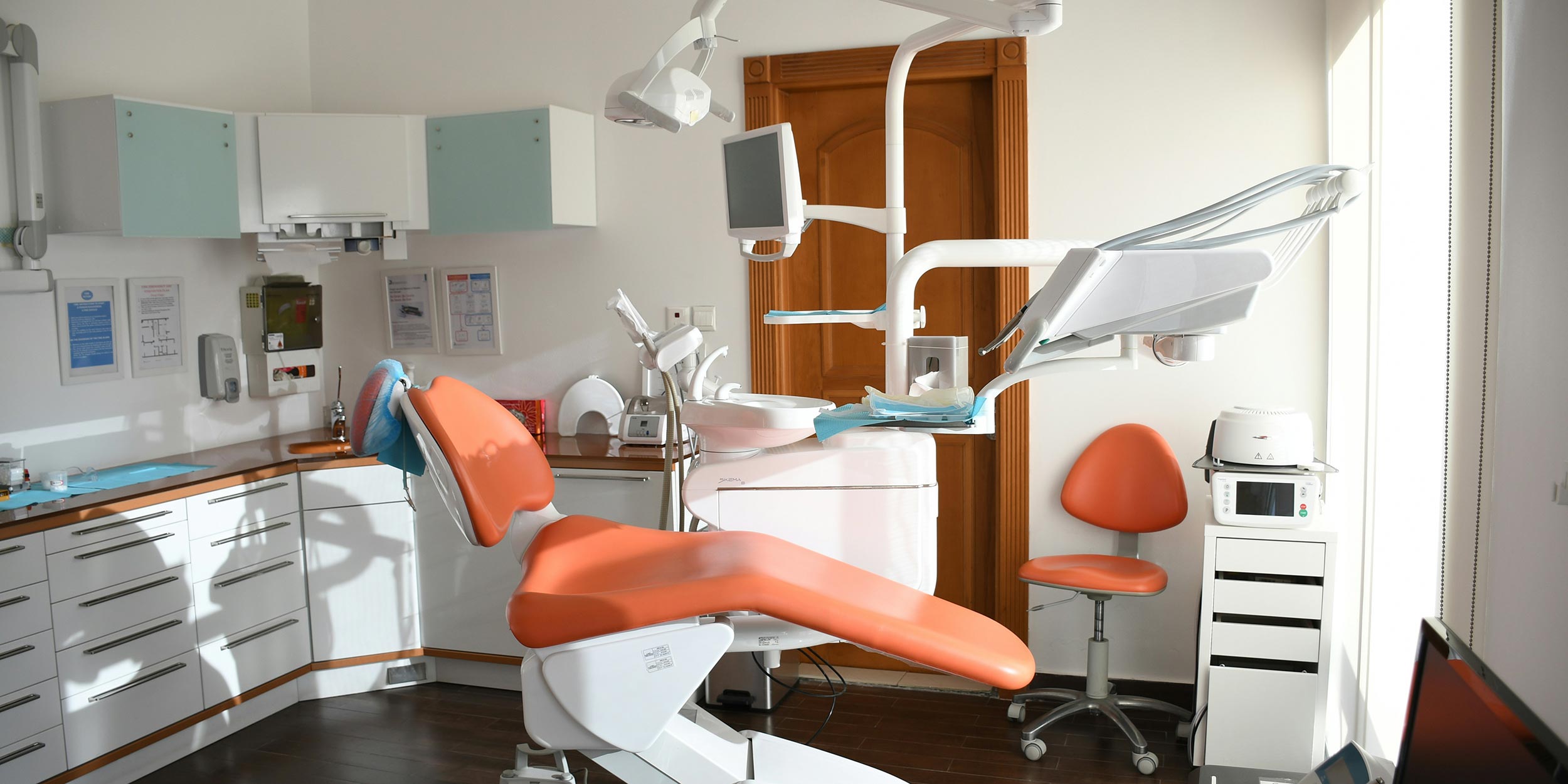 Bright dental office with orange chair, tools, and mounted monitor