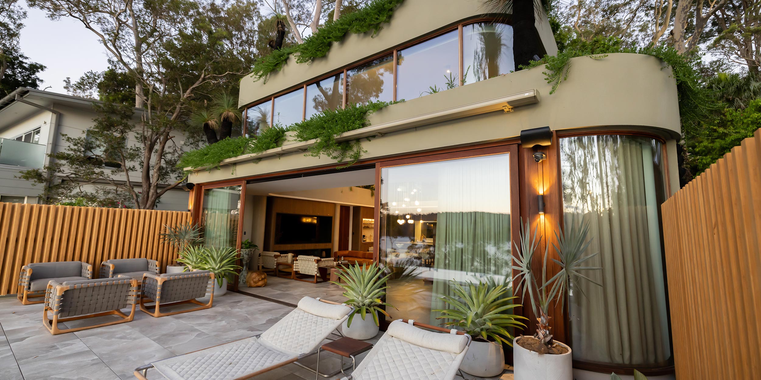 Modern home exterior with open patio and lounge seating surrounded by trees