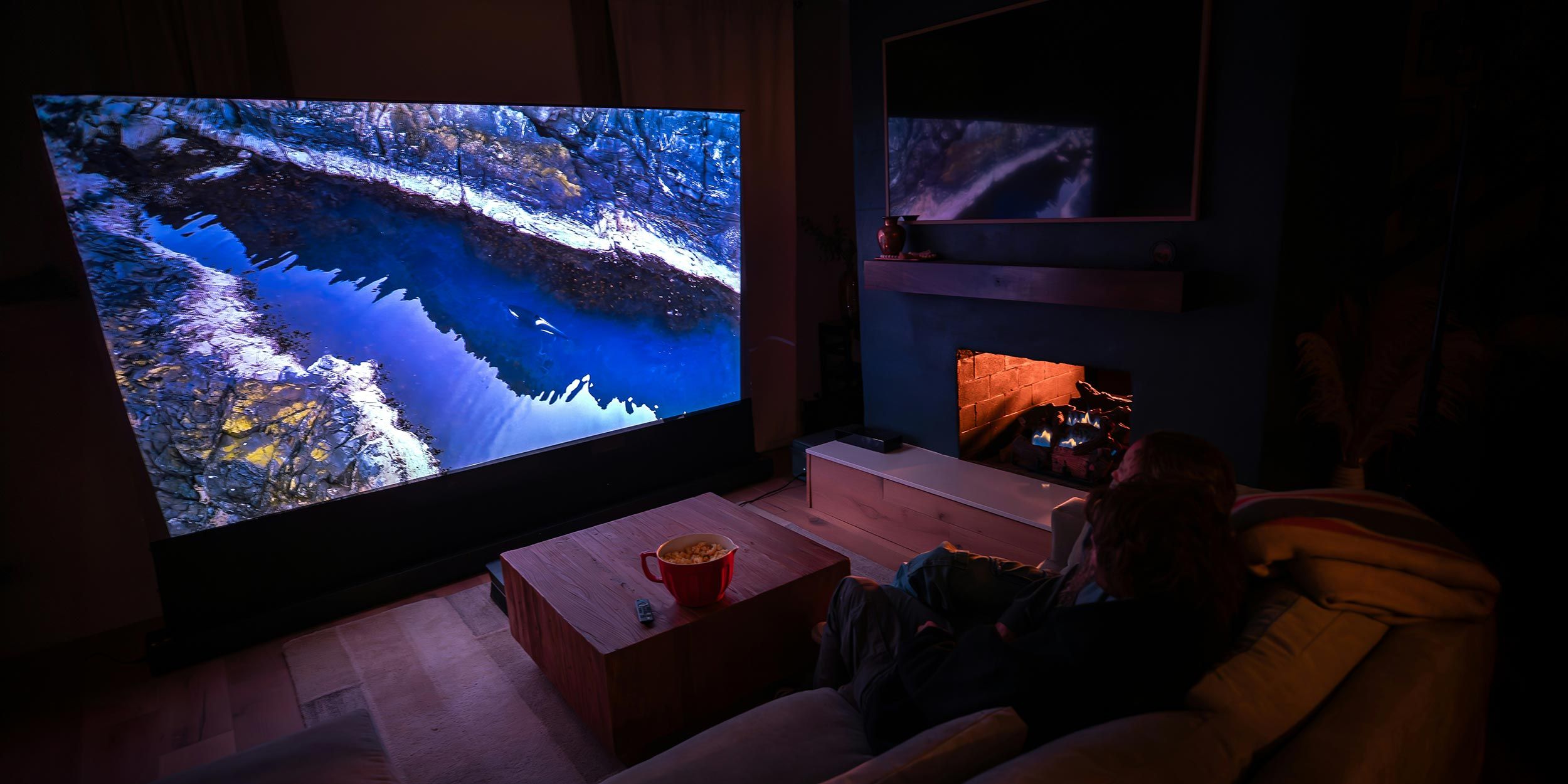 Couple watching large screen TV in dark home theater with fireplace